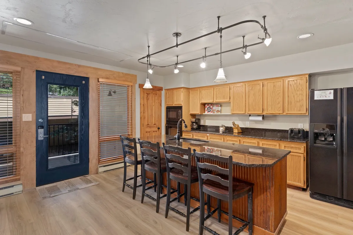This view features a kitchen island with bar stools, modern cabinetry, stylish lighting, and a visible doorway that connects the kitchen to other areas, emphasizing the open-concept design.