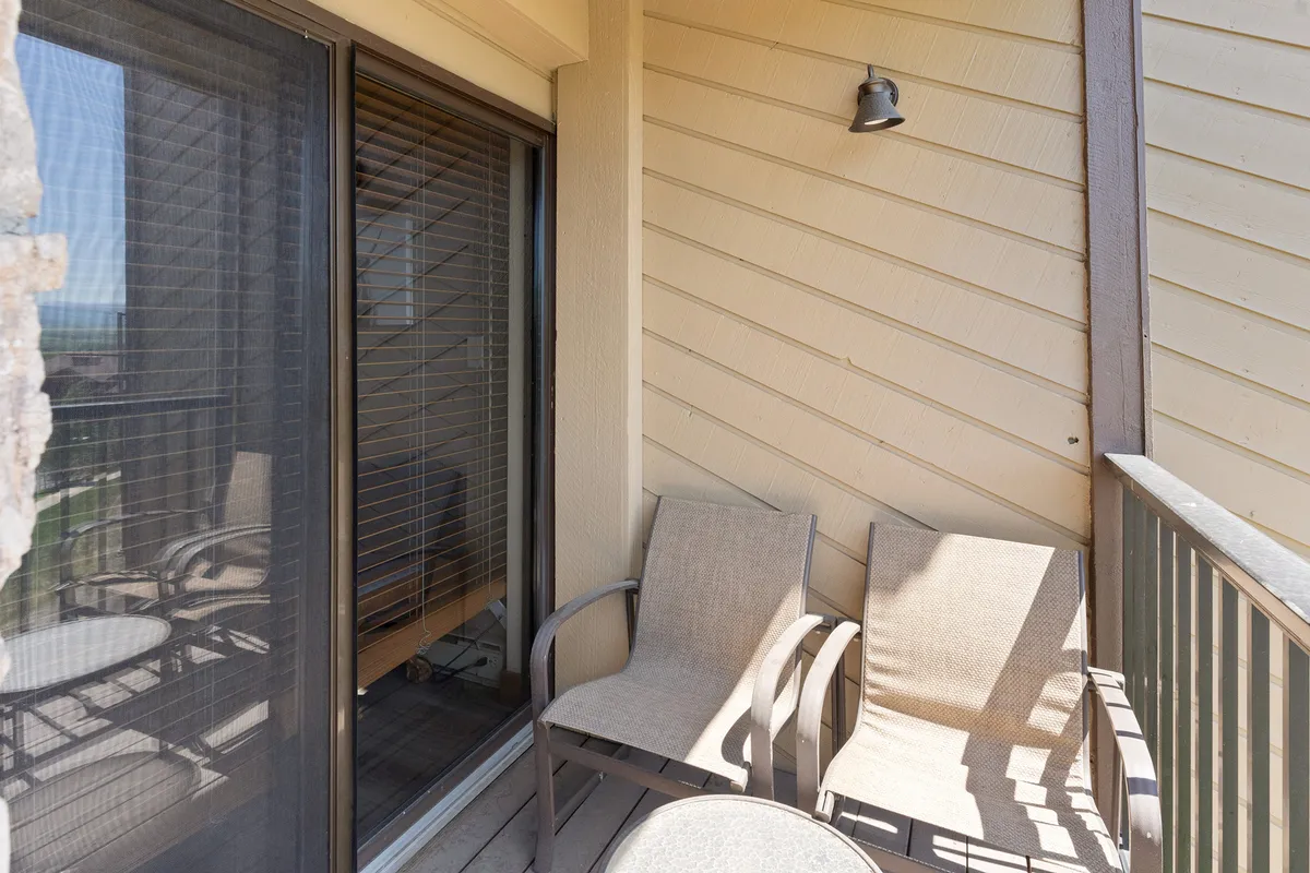 A peaceful patio scene with two comfortable chairs and a small table positioned by a glass sliding door. The setup offers a tranquil atmosphere for morning coffee or evening relaxation, looking out at natural Steamboat scenery.