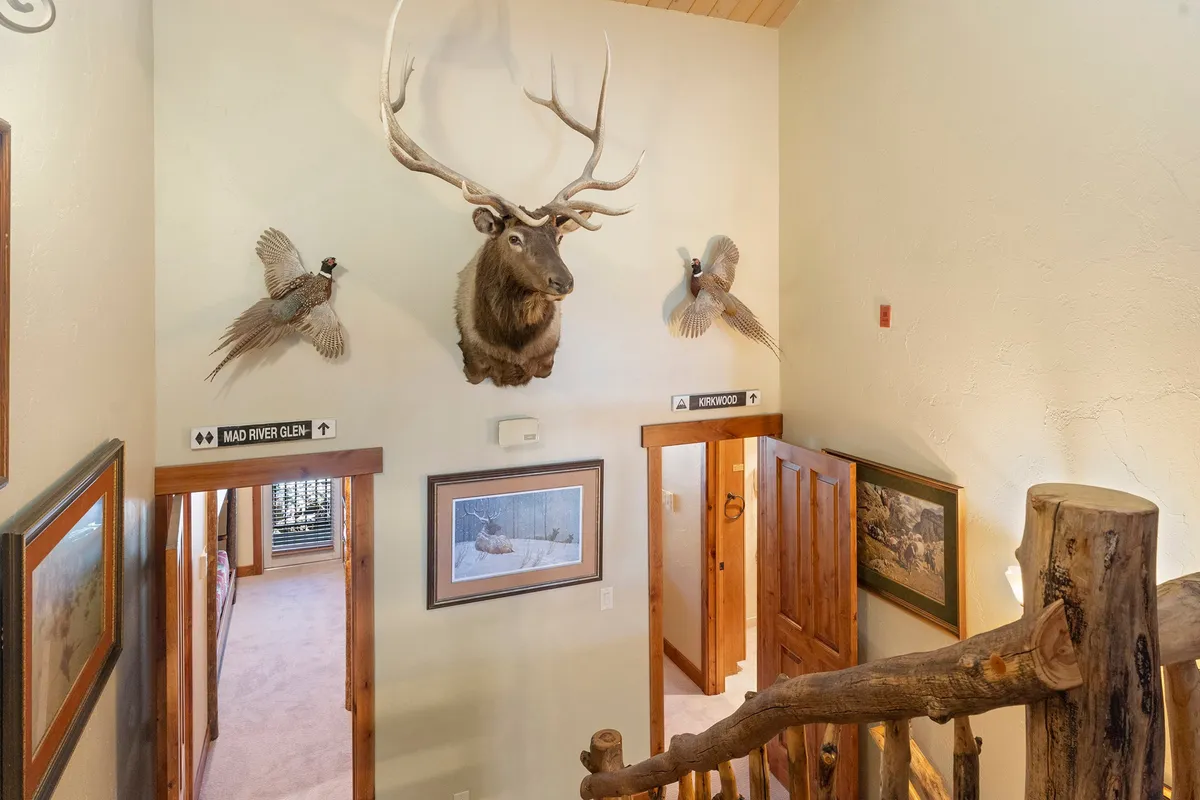 This image captures the home's inviting entryway, featuring antlered mounts, framed wildlife art, and rustic wooden doors. The décor hints at a connection to outdoor adventures and seasonal experiences, setting the tone for both winter and summer getaways.
