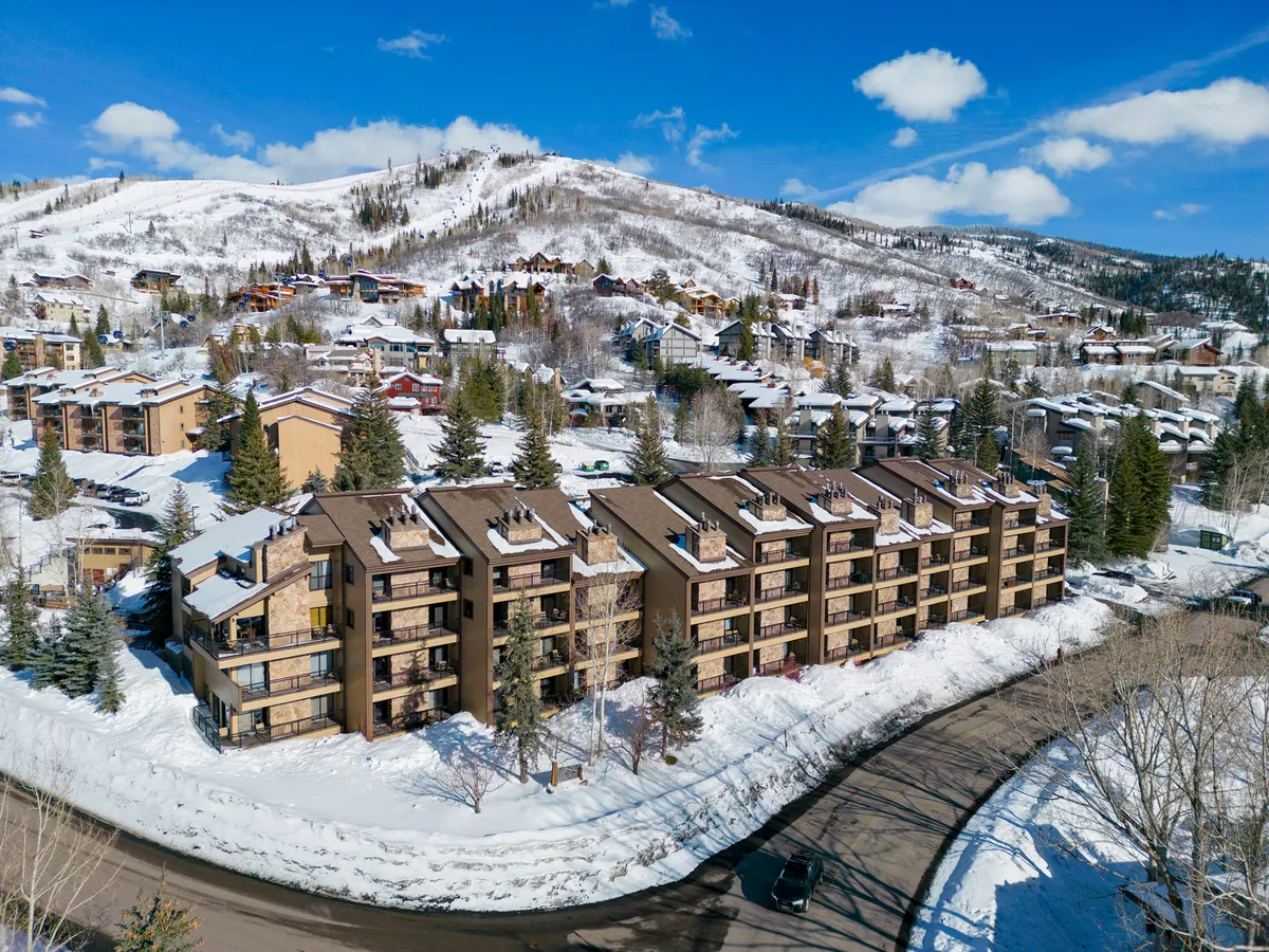 A panoramic exterior shot capturing snow-covered mountains, pine trees, and residential buildings nestled along a curved road. The scene conveys a sense of adventure and tranquility, set against the backdrop of Steamboat’s renowned winter landscape.