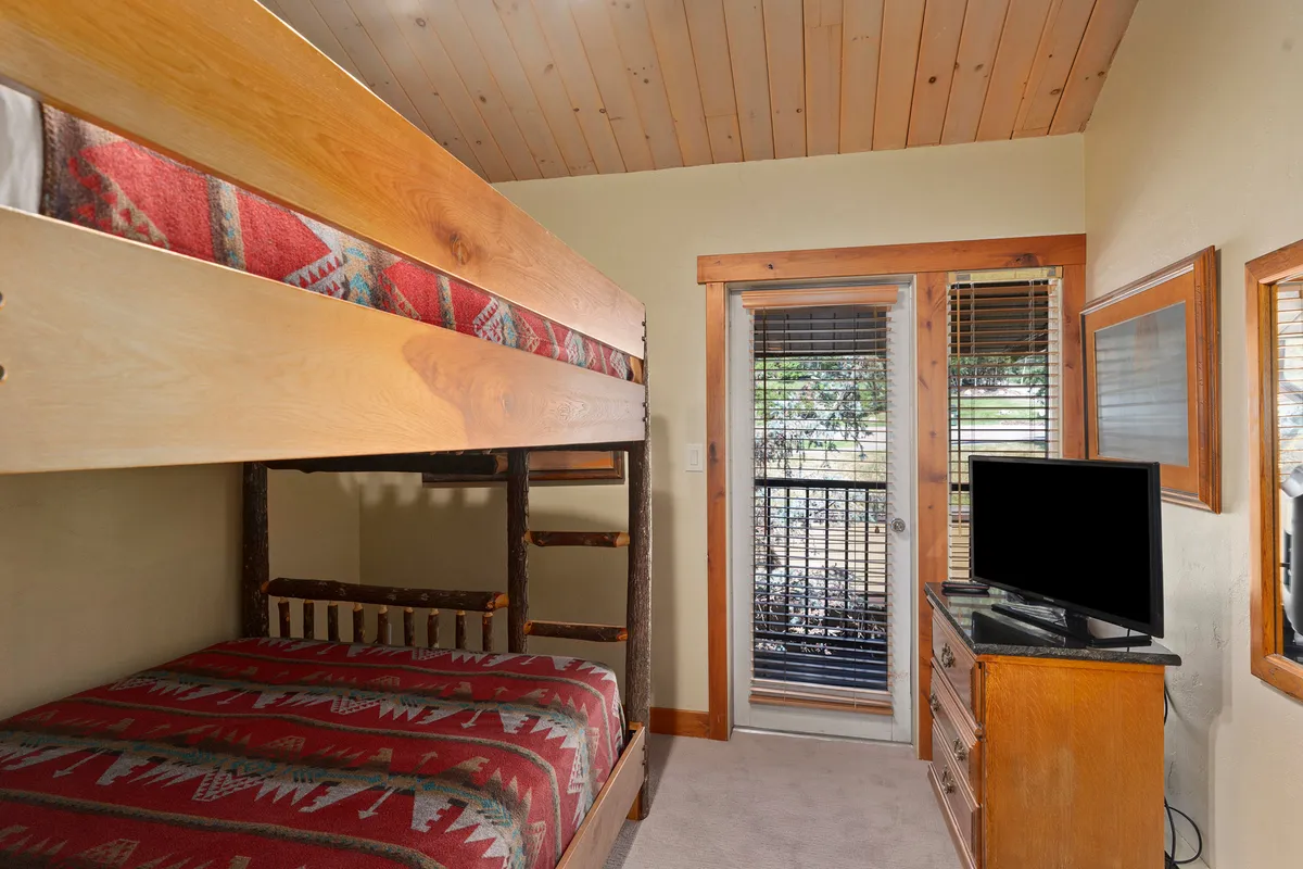 A welcoming bunk room with a bunk bed, a window offering natural light and views, television, and a wooden dresser. The setting is inviting and family-friendly, ideal for relaxing or watching TV after a day on the mountain.