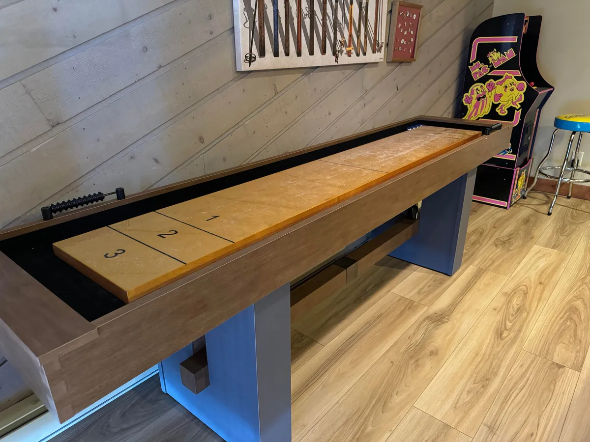 A vibrant game lounge scene featuring a shuffleboard table, an arcade game, and wall art, creating an inviting space for fun and friendly competition.