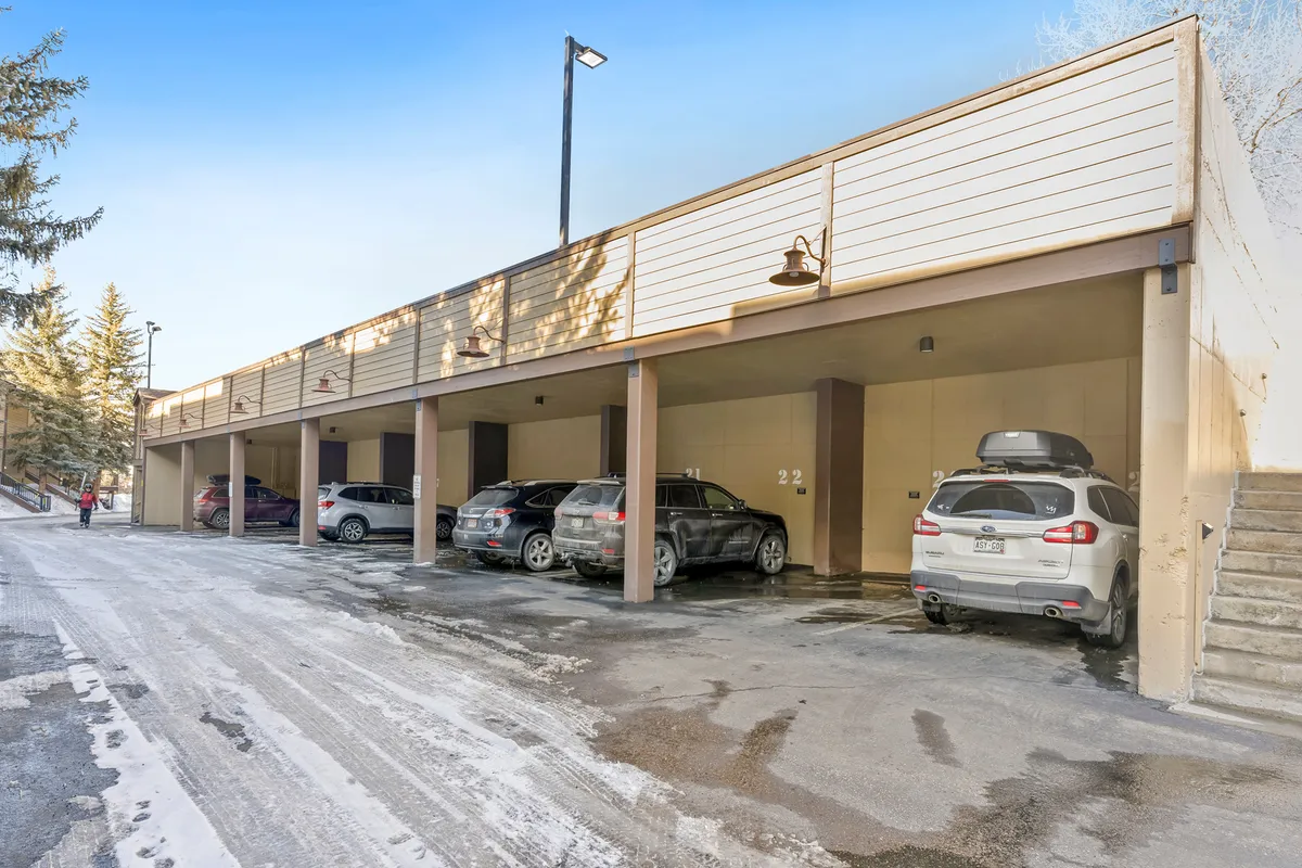 A covered parking area surrounded by snowy trees, with several cars and walkways leading to the accommodations. The image conveys convenience, easy access for larger groups, and a sense of community within the property grounds.