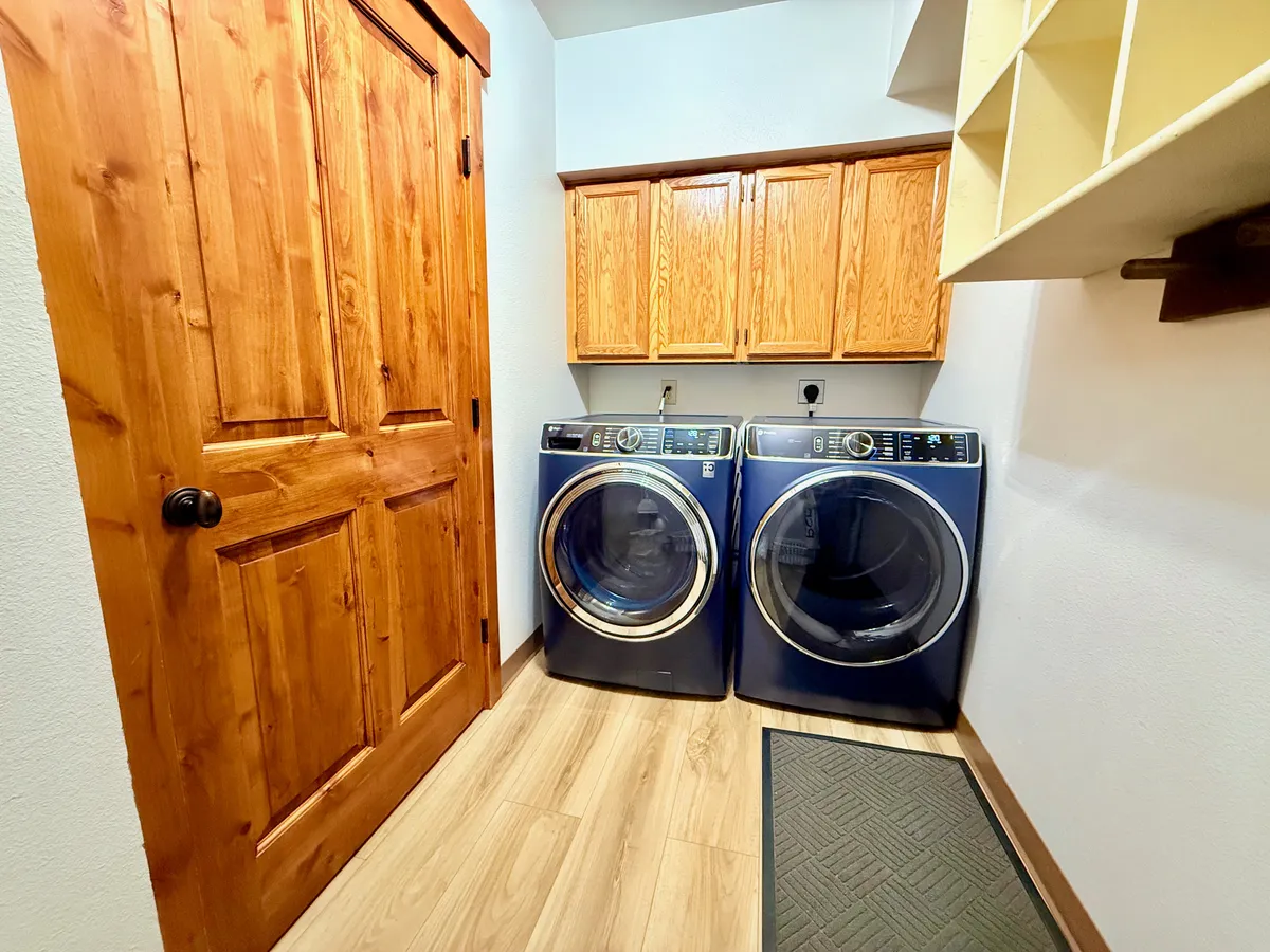 A bright and functional laundry area with a full-size washer and dryer, complemented by wooden cabinets and a sturdy door, offering a dedicated space for household chores.