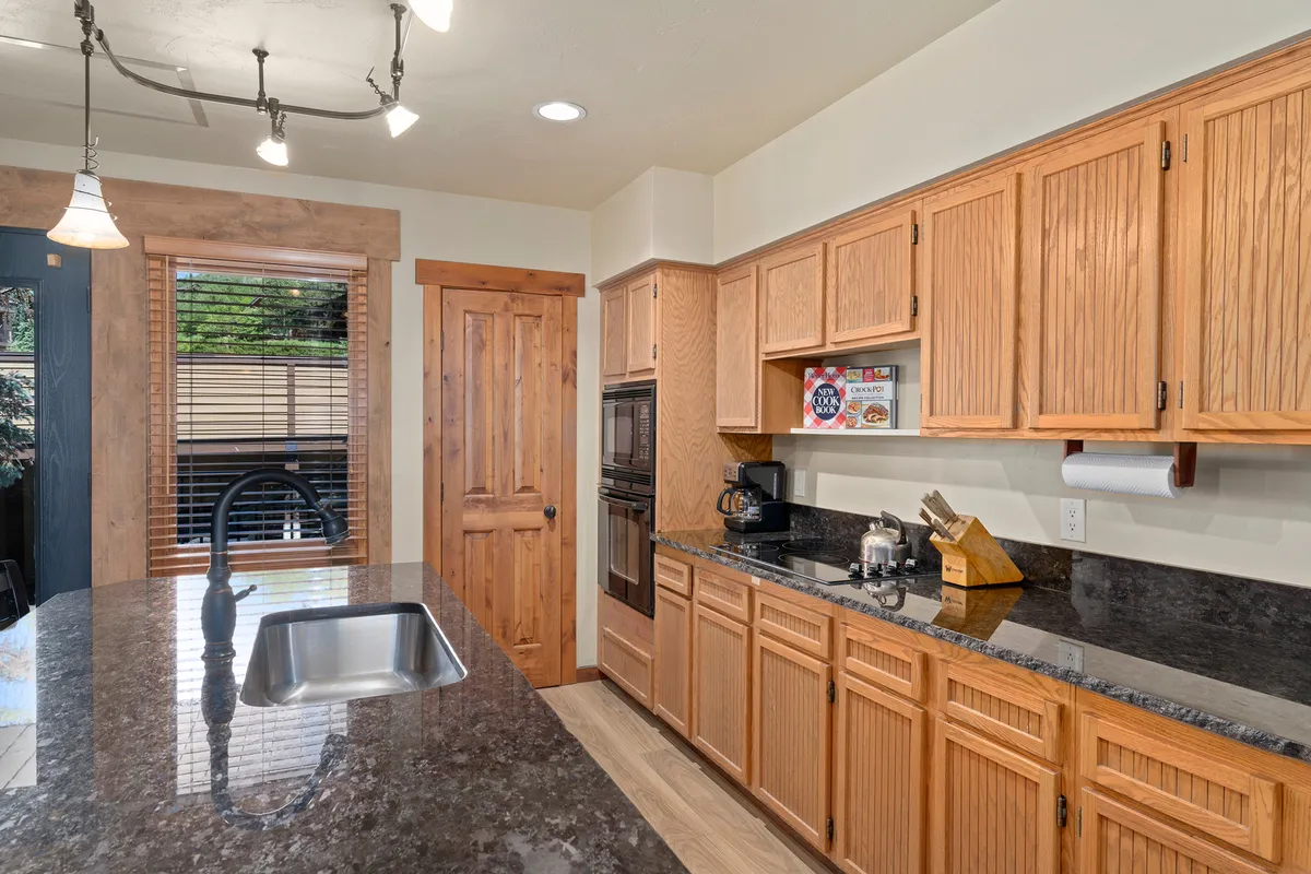 A cozy kitchen scene with a granite countertop island, warm wood cabinets, and inviting ambiance. The layout encourages both cooking and casual gatherings, reflecting a space designed for family and group activities.