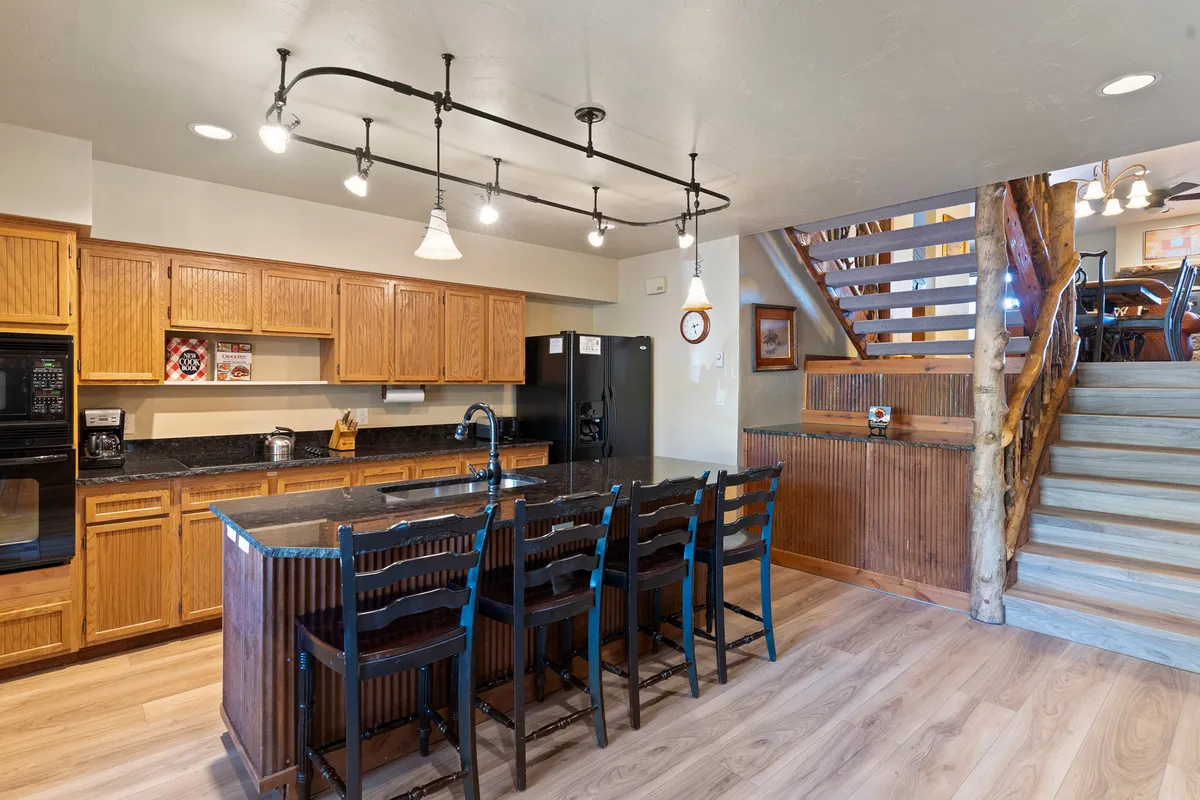 This image showcases a spacious kitchen with a prominent island and seating, stainless steel appliances, and warm wooden cabinetry. The lighting fixtures add a cozy touch, while the open layout hints at connectivity to adjacent living spaces.