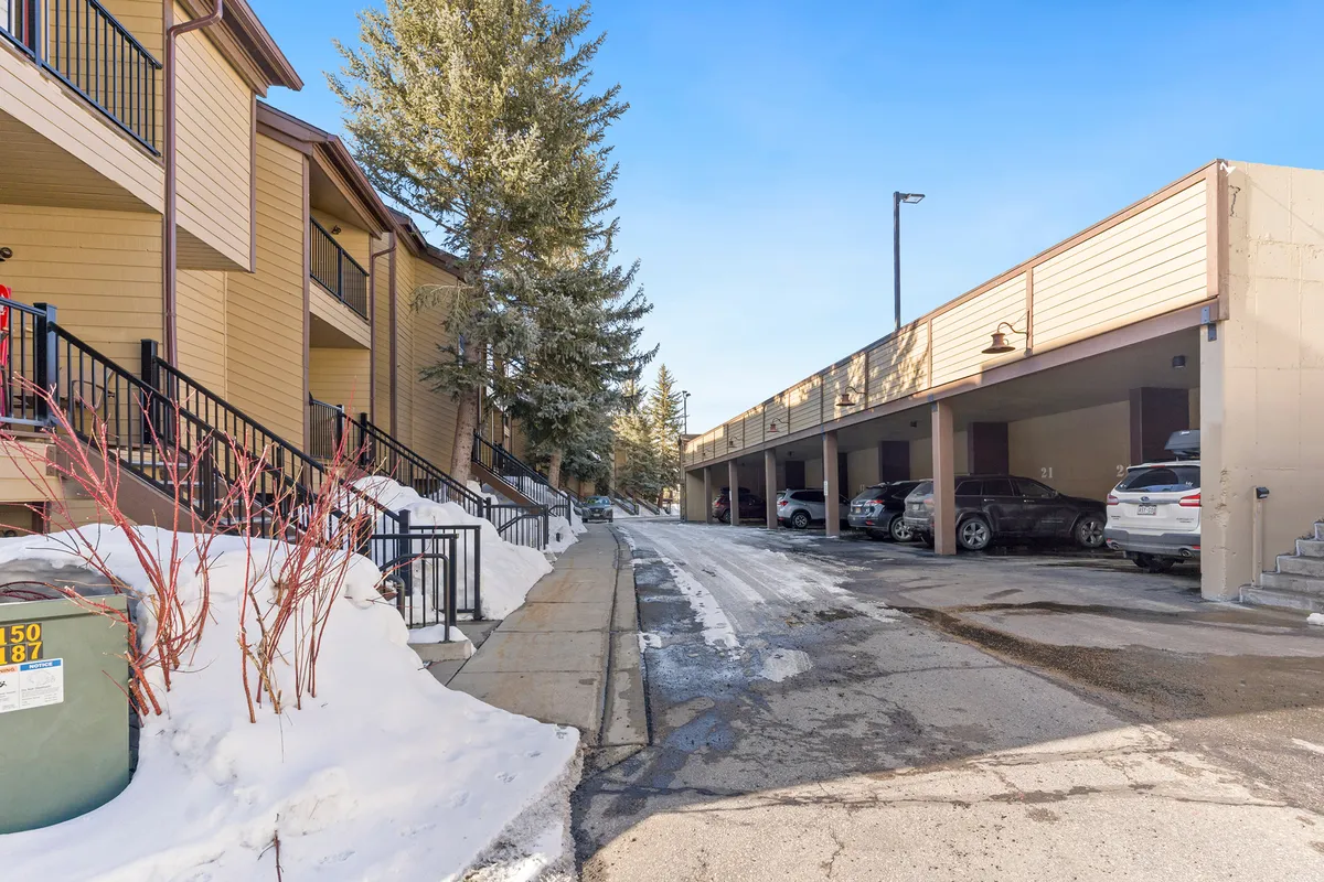 A welcoming winter exterior featuring a snow-covered ground, stairs leading to individual apartments, and a nearby parking area. The scene sets a tranquil and communal tone, hinting at easy access and the inviting nature of the accommodations.
