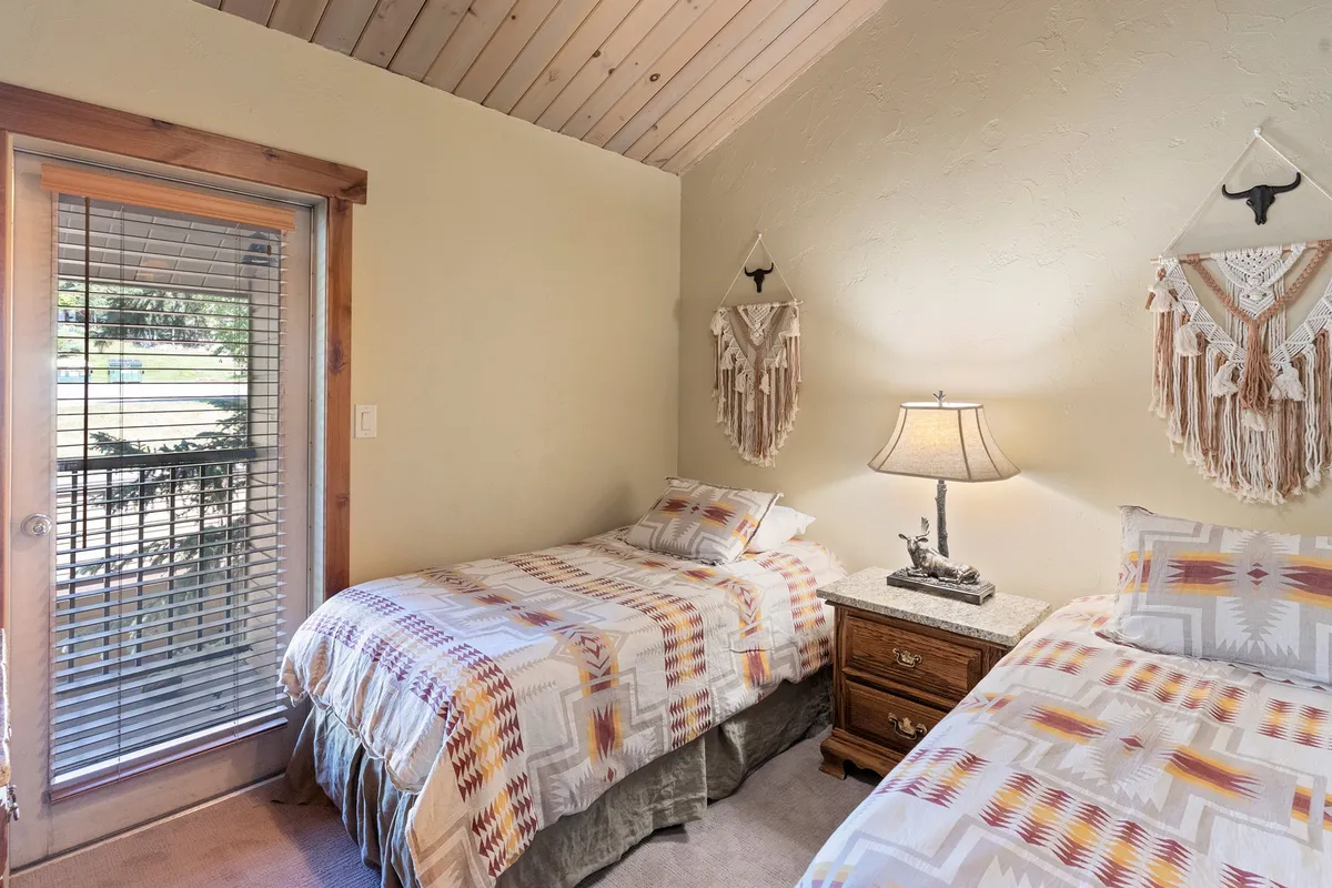 A serene twin bedroom featuring twin beds with patterned bedding, decorative wall hangings, and a table lamp. The room is bright and inviting, perfect for kids or guests seeking comfort and privacy.