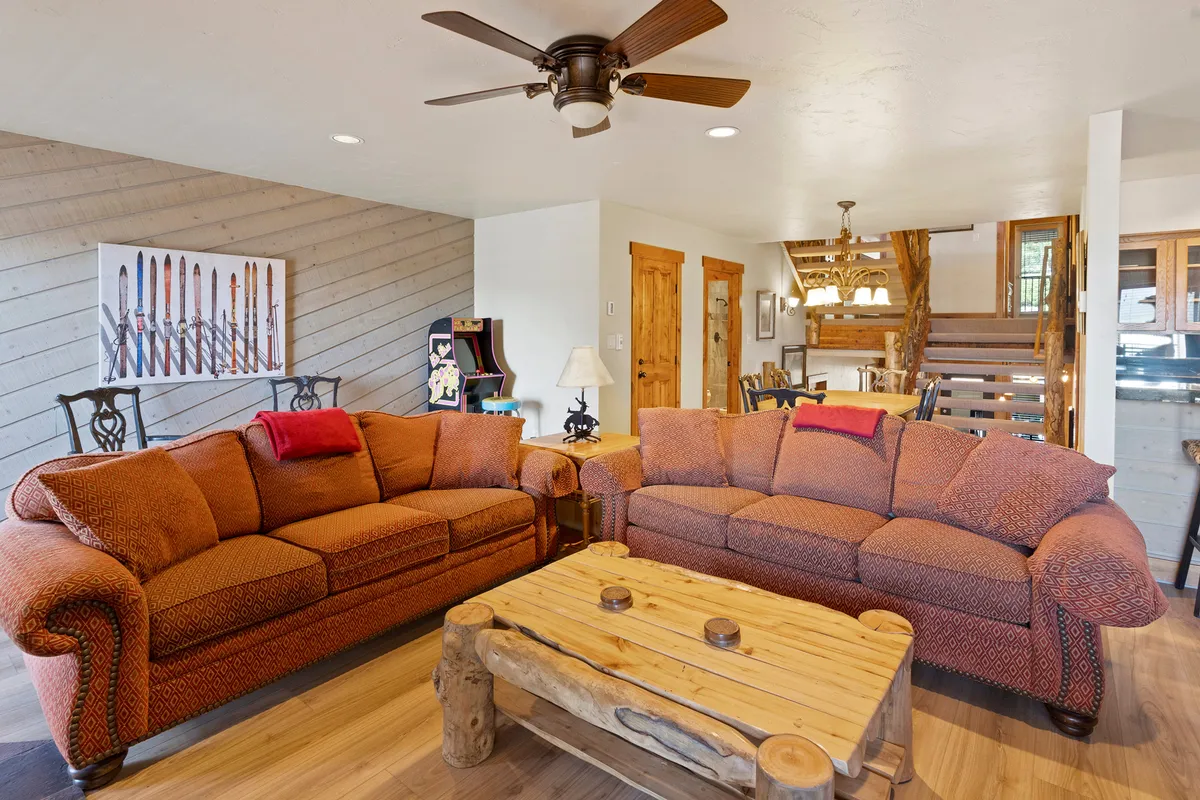 A warm, open-plan living and dining space with two large sofas surrounding a wooden coffee table, set against a backdrop of inviting artwork. The dining area is visible in the background, suggesting a seamless flow for group gatherings and meals.