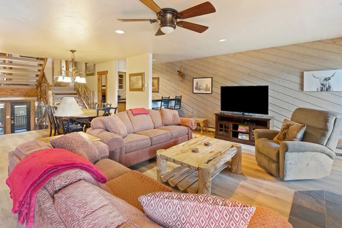 A spacious, welcoming living room with comfortable sofas arranged around a rustic wooden coffee table, and a TV unit ready for family game nights or movies. The fireplace in the background adds an extra layer of warmth and coziness—perfect for evenings spent together after a day outdoors.
